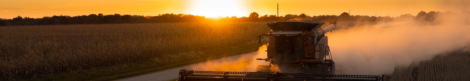 Combine harvester working in the soybean field against a clear sky at sunset in Missouri